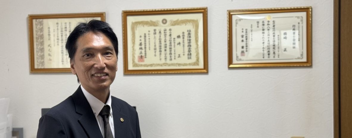 事務所に掲げた登録証の前に立つ代表 橋崎正